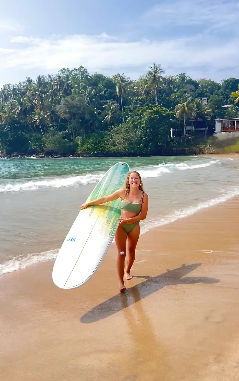 Evelyne läuft mit einem Longboard am Strand von Sri Lanka